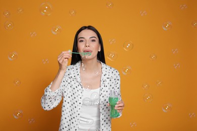 Young woman blowing soap bubbles on yellow background