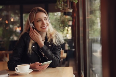 Young woman with headphones and smartphone listening to music in cafe