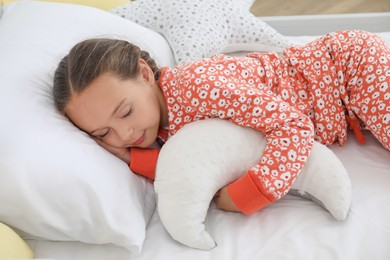 Cute girl in pajamas sleeping with moon shaped pillow at home