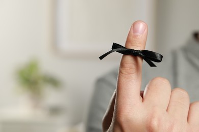 Photo of Man showing index finger with black tied bow as reminder on blurred background, closeup. Space for text
