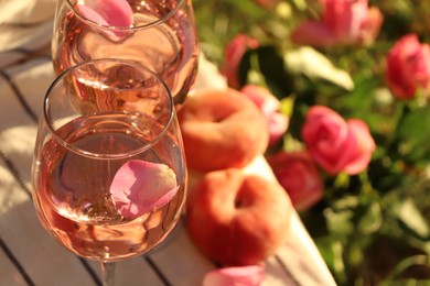 Photo of Glasses of delicious rose wine with petals on white picnic blanket outside. Space for text