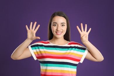 Woman showing number nine with her hands on purple background
