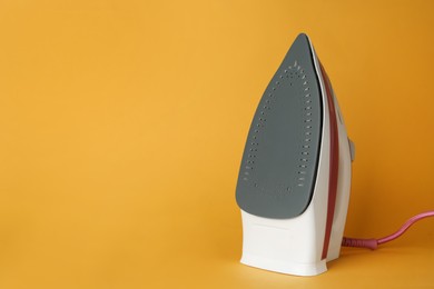 One modern iron on orange background, space for text. Home appliance