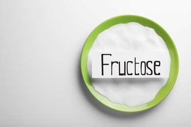 Photo of Bowl of sugar and paper sheet with word Fructose on white background, top view. Space for text