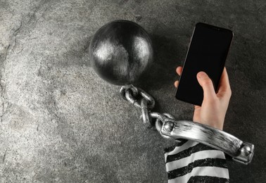 Prisoner shackled with ball and chain holding smartphone at grey table, top view