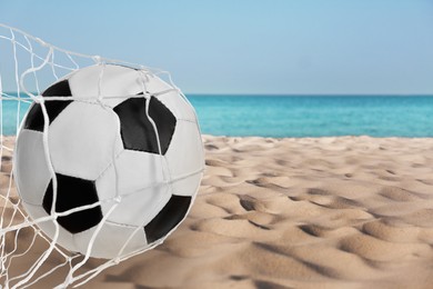 Soccer ball in net on sandy coast near sea. Beach football