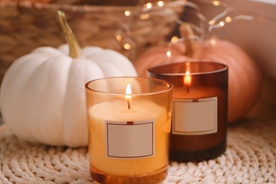 Scented candles and pumpkins on wicker mat indoors, closeup