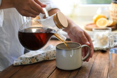 Woman pouring delicious tea into cup at wooden table, closeup