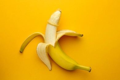Banana with condom on orange background, top view. Safe sex concept