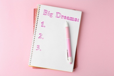Notebook with dreams list and pen on pink table, top view