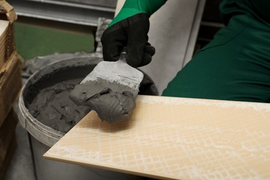 Worker applying adhesive mix on ceramic tile with spatula, closeup
