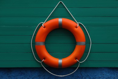 Orange lifebuoy hanging on green wooden board. Rescue equipment