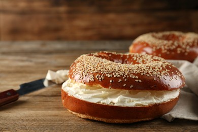 Delicious bagel with cream cheese on wooden table, closeup