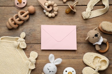Baby shower party. Envelope surrounded by stuff for child on wooden background, flat lay