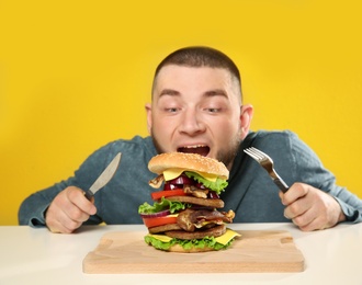 Photo of Young man with cutlery and tasty huge burger at table