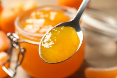 Teaspoon with tasty tangerine jam over table, closeup