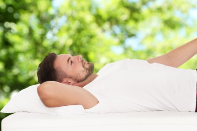 Man lying on comfortable mattress against blurred green background, bokeh effect. Sleep well - stay healthy