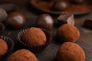 Delicious chocolate truffles powdered with cocoa on wooden board, closeup