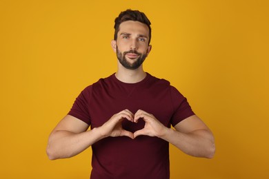 Man making heart with hands on yellow background