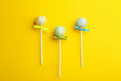 Different tasty cake pops on yellow background, flat lay