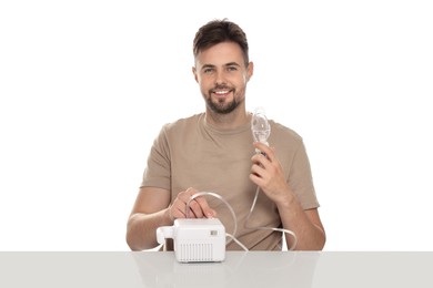 Photo of Man turning on nebulizer for inhalation at table against white background