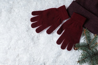 Stylish woolen gloves, hat and fir branches on artificial snow, flat lay. Space for text