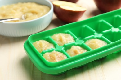 Photo of Apple puree in ice cube tray ready for freezing with fresh apple fruits on wooden table, closeup