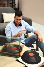 Happy man drinking tea while listening to music with turntable at home