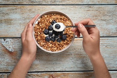 Photo of Woman eating yogurt with granola and blueberries on old wooden table, top view