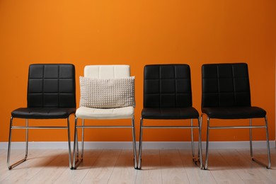 Photo of Black chairs with white one and pillow near orange wall. Recruiter searching employee