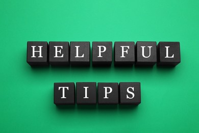Photo of Phrase Helpful Tips made of black cubes with letters on green background, top view