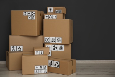 Cardboard boxes with different packaging symbols on floor near black wall. Parcel delivery
