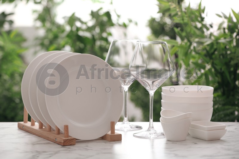 Photo of Set of clean dishware and wineglasses on white table against blurred background