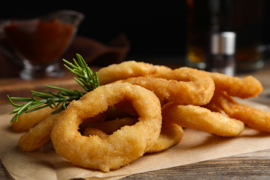 Pile of delicious crunchy fried onion rings with rosemary on wooden table, closeup