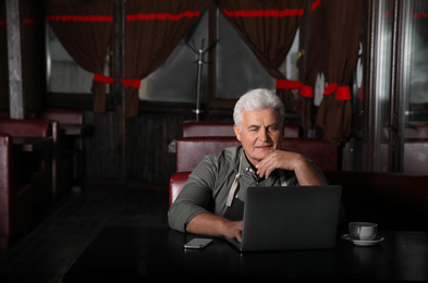 Senior business owner working with laptop in his restaurant