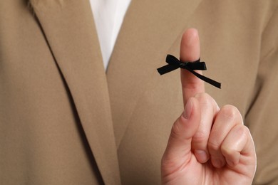 Photo of Woman in beige suit showing index finger with tied black bow as reminder, closeup
