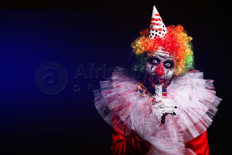 Photo of Terrifying clown on dark background, space for text. Halloween party costume