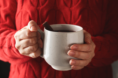 Woman holding cup of mulled wine with cinnamon, closeup. Winter drink