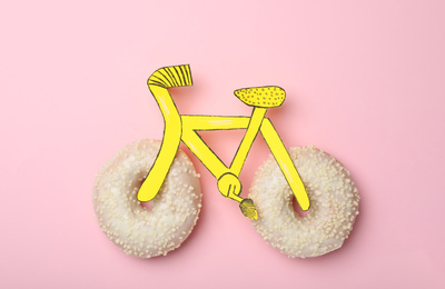 Bicycle made with donuts and paper on pink background, top view