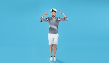 Strong sailor showing biceps on light blue background