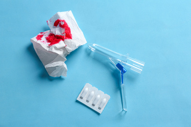 Anoscope, suppositories and toilet paper with blood on light blue background, flat lay. Hemorrhoid treatment