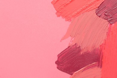 Smears of different beautiful lipsticks on pink background, top view. Space for text