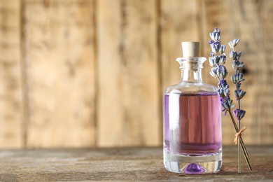 Photo of Bottle of natural essential oil and lavender flowers on wooden background. Space for text