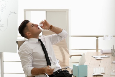 Photo of Ill businessman using nasal drops in office