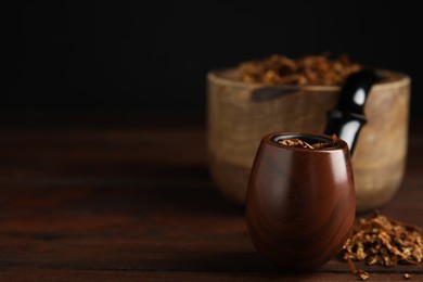 Smoking pipe and dry tobacco on wooden table against dark background, closeup. Space for text