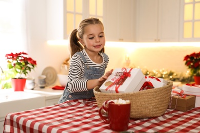 Photo of Cute little girl taking gift from Christmas advent calendar at table in kitchen