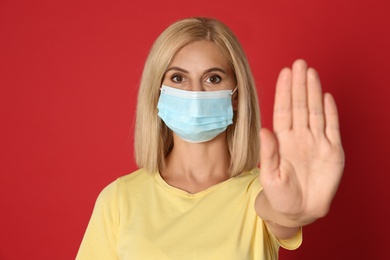 Woman in protective mask showing stop gesture on red background. Prevent spreading of coronavirus