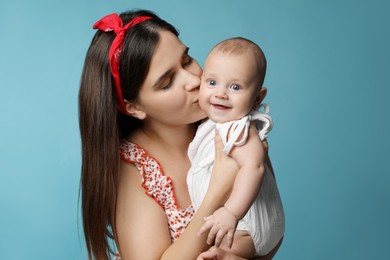Beautiful mother kissing her cute baby on turquoise background