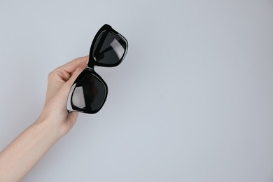 Photo of Woman holding stylish sunglasses on light background, closeup. Space for text