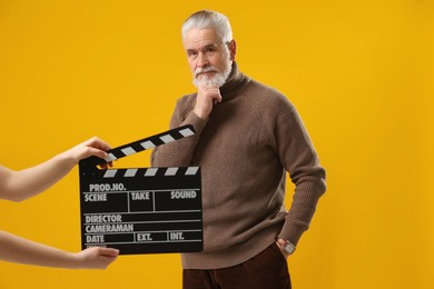Photo of Senior actor performing while second assistant camera holding clapperboard on yellow background. Film industry